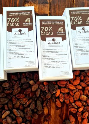 Row of white chocolate boxes labeled 70% cacao on a wooden table, surrounded by cacao beans.
