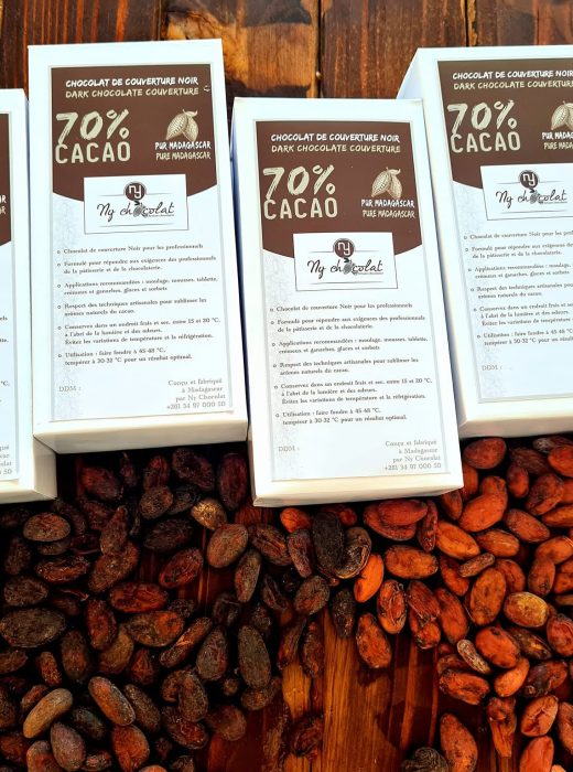 Row of white chocolate boxes labeled 70% cacao on a wooden table, surrounded by cacao beans.
